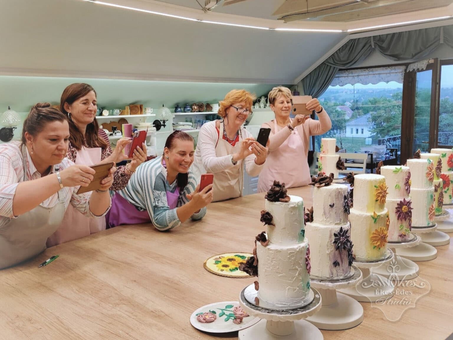 Csokoládés késsel festett tortadíszítő tanfolyam végé a boldog résztvevők az elkészült tortákat fotózzák – Ékes-Édes Stúdió, tortadíszítő tanfolyam
