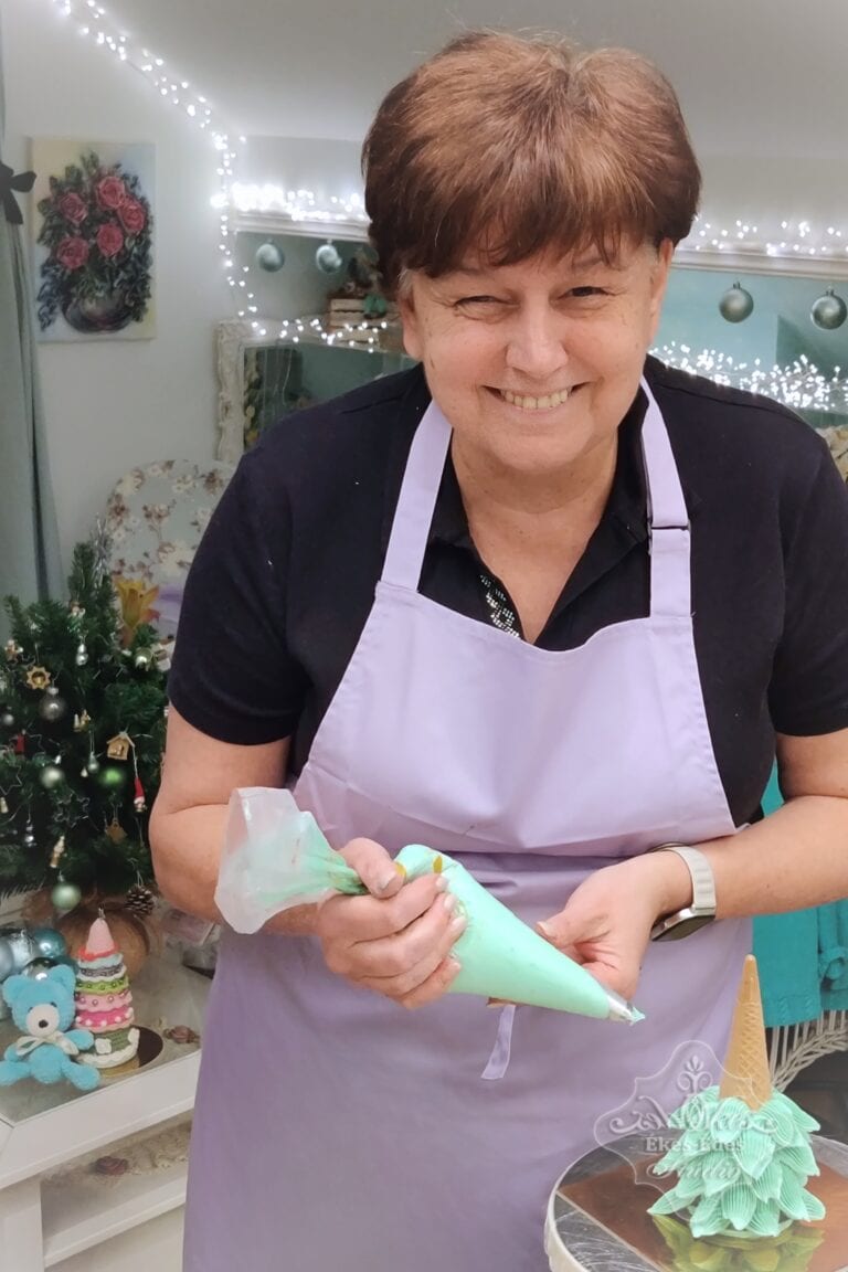 Ünnepi hangulatú teremben egy mosolygó tanuló, fenyőfa alakú pillecukrot készít karácsonyi ajándékba habzsákkal a kezében, az Ékes-Édes Stúdióban.