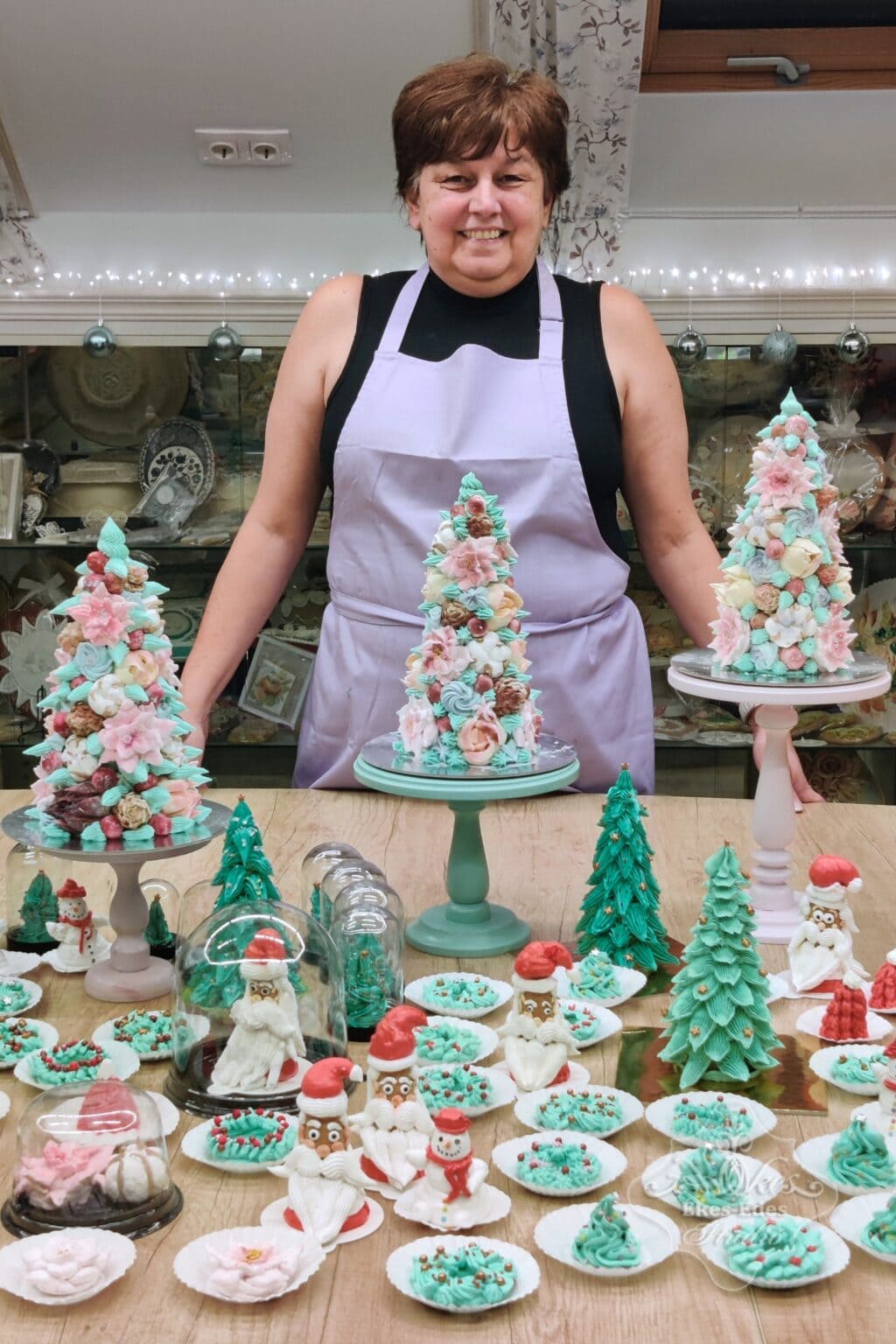 Ékes-Édes Stúdió karácsonyi pillecukor tanfolyamon készült termékek színes csoportja az asztalon és mögöttük egy vidám és büszke résztvevő áll.