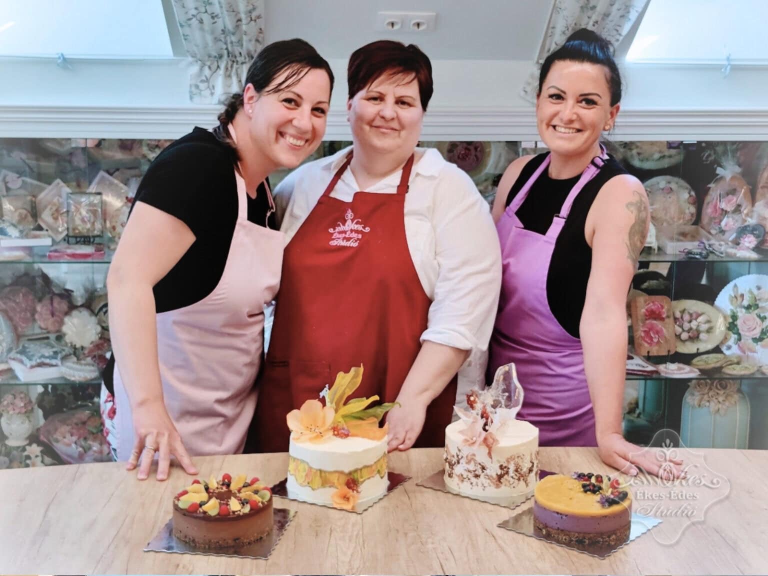 A képen két tanuló és az oktató látható, akik a cukrászati műhelyben állnak, a kész tortákat mutatva – Ékes-Édes Stúdió, mentes cukrászat tanfolyam.