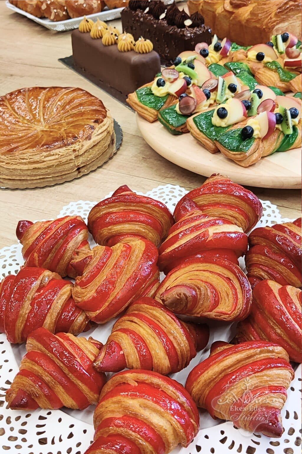 Tanfolyam végén az asztalra kirakott elkészült francia péksütemények színes csoportja látható, előtérben piros croissantokkal.