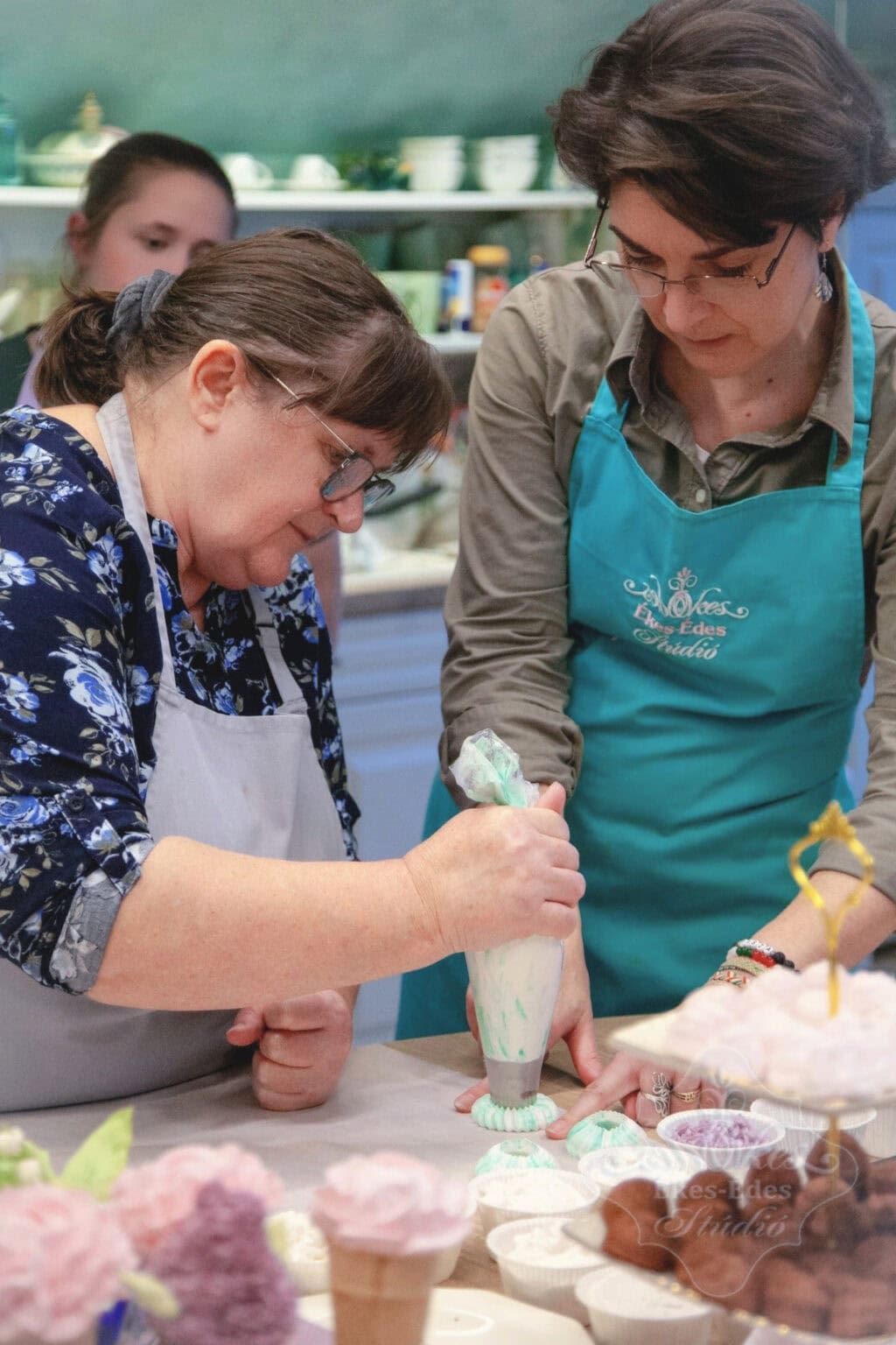 Oktató és tanuló együttműködése, a tanuló pillecukor karikákat készít habzsákkal és szultáncsővel, az oktató instrukciói segítségével.