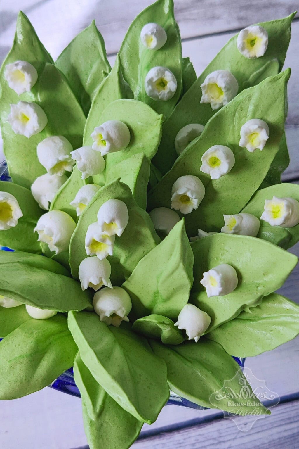 Gyöngyvirág csokor zöld levelekkel és fehér virágokkal pillecukorból közelről fotózva, ideális ajándék vagy dekoráció.