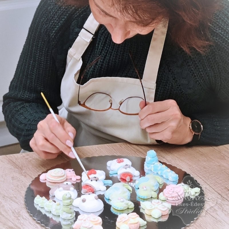 Kézműves pillecukor figurák készítése közben egy résztvevő a fotón közelről, ecsettel színezi a figuráit az ékes-édes stúdió tanfolyamán.
