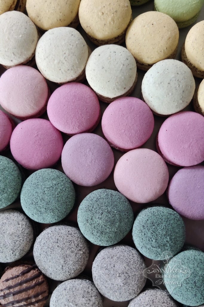 Színes macaronok feülről fotózva szorosan egymás mellé rendezve: diós, mákos, kókuszos és mandulás tésztákból.