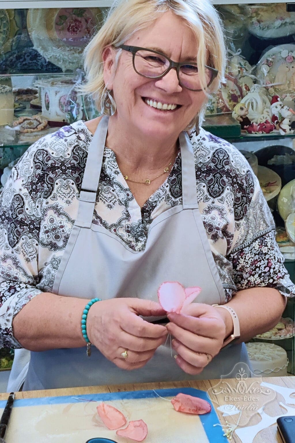 Ékes-Édes Stúdió mentes cukrászat tanfolyamán résztvevő mosolyog a képen ostyavirág tortadekoráció készítés közben.