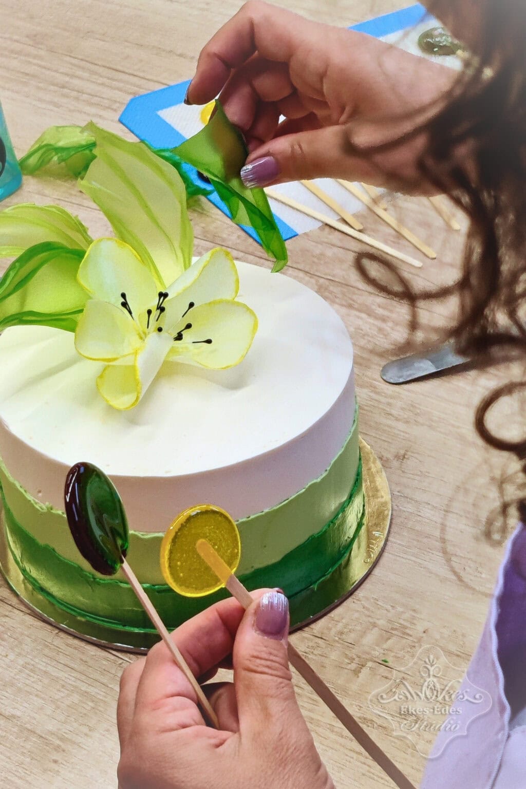 Színes vitorlákat, ostyavirágokat és izomalt poppokat alkalmaz a mentes tortája díszítésében az Ékes-Édes Stúdió mentes cukrászat tanfolyamának résztvevője.