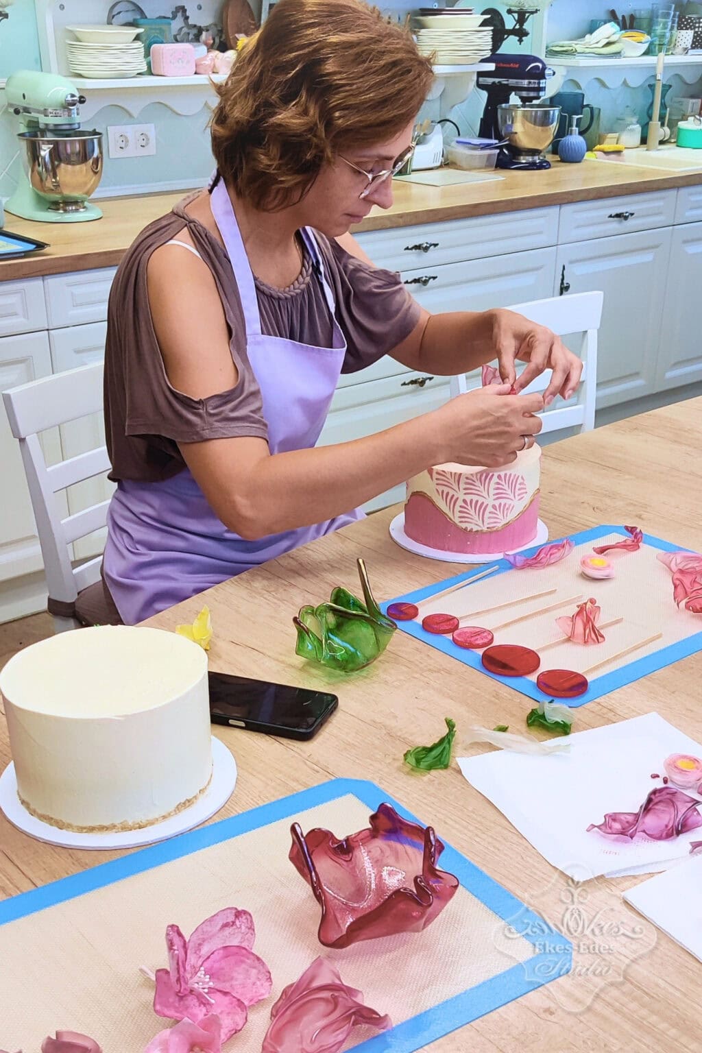 Tortadíszítés mentes cukrász tanfolyamon. ostyavirágok, vitorlák és izomalt kosárral az előtérben, barátságos környezetben.