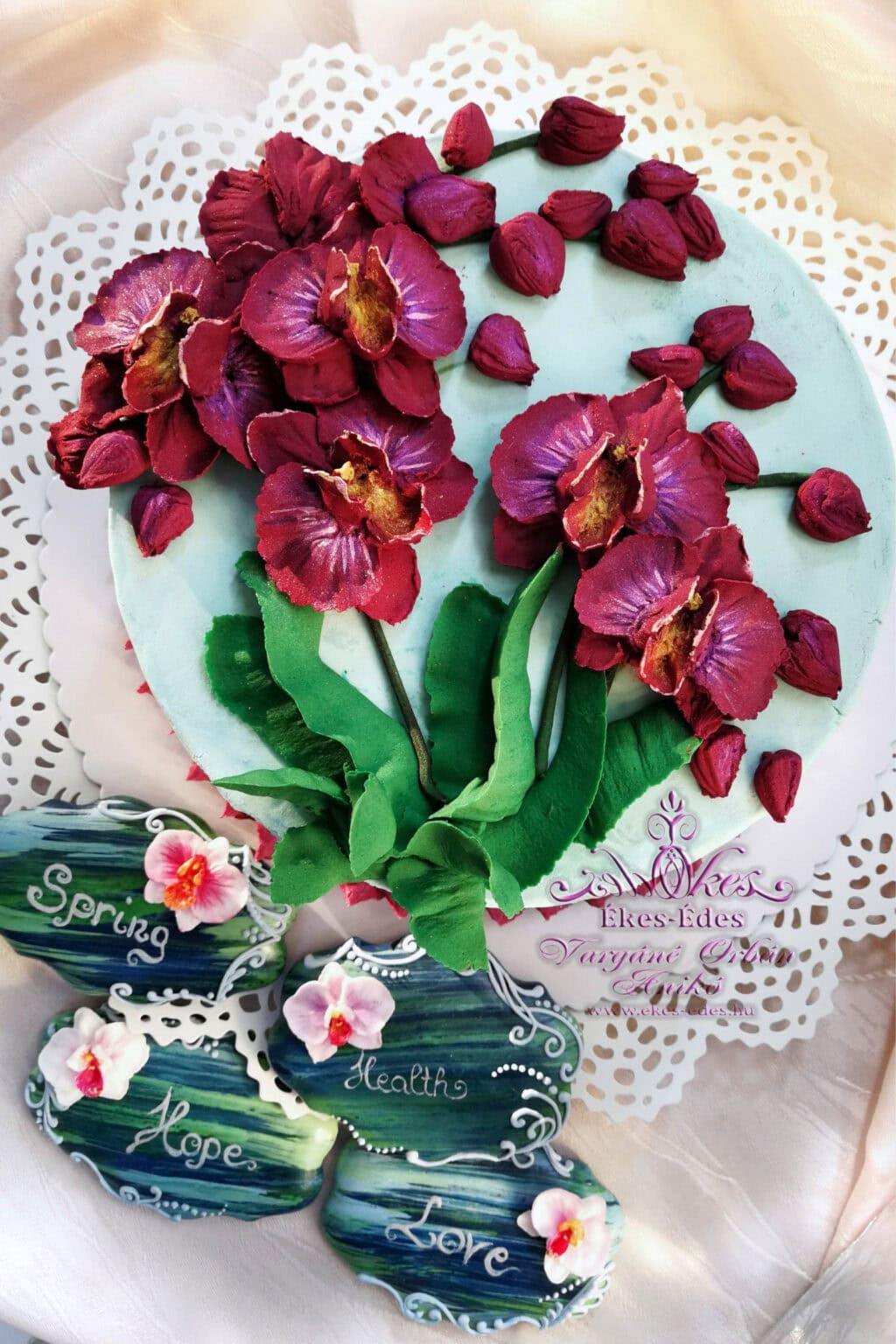 Orchideás babkrém torta, részletes virágdíszítéssel. Az előtérben cukormázzal díszített mézeskalácsokkal.