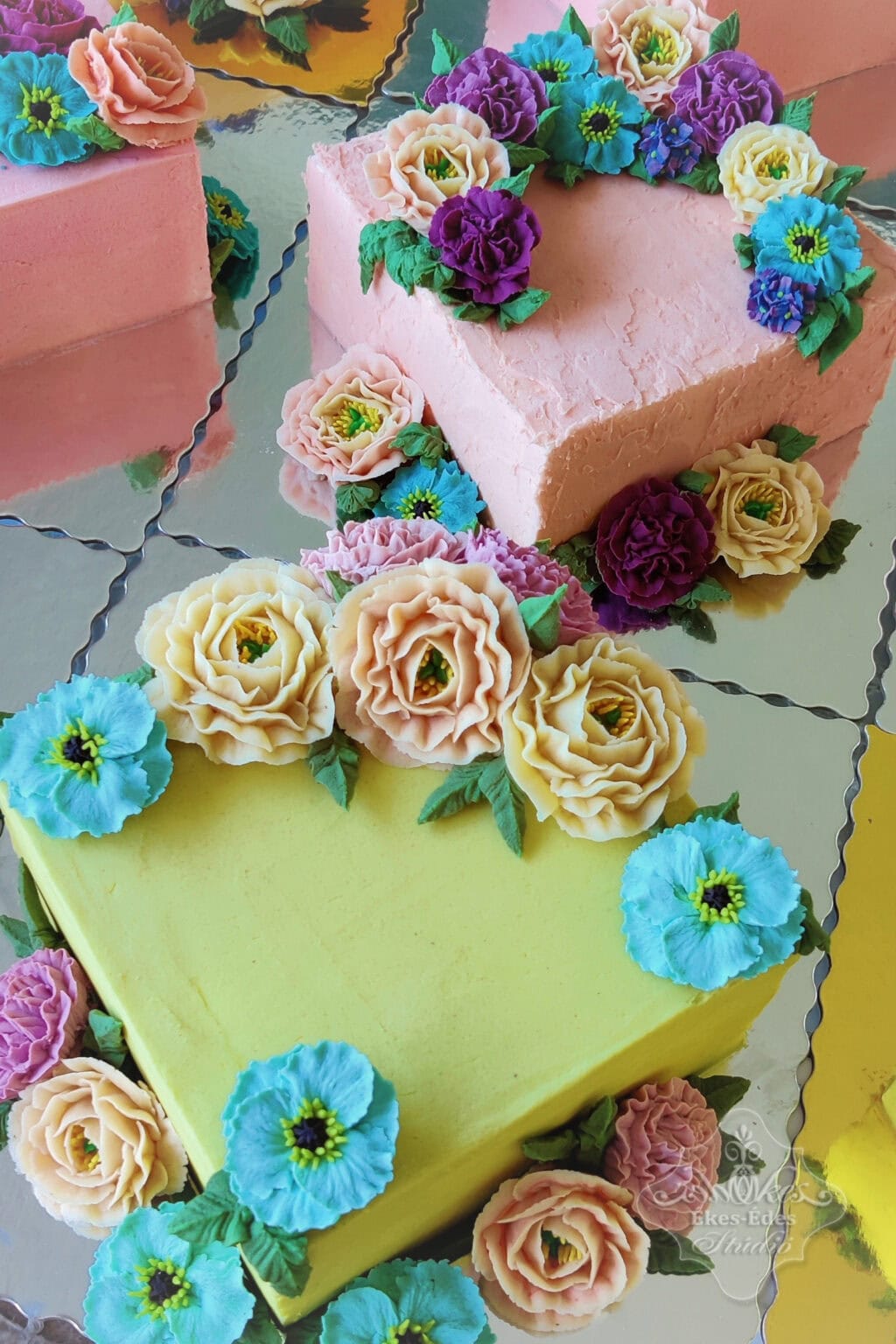 Két szép formájú, színes virágokkal díszített babkrémes torta.