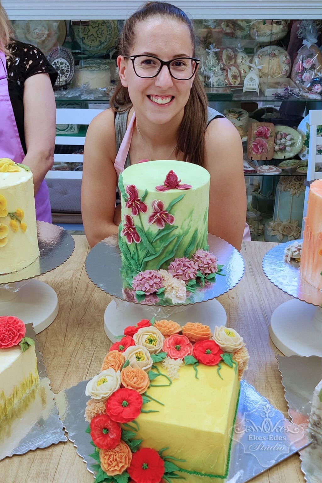 két színes babkrémmel készült tortadekoráció és büszke készítőjük a tanfolyam végi fotózáson.