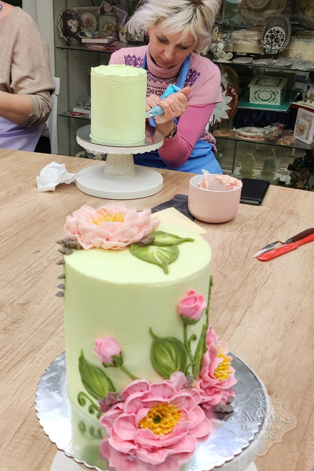 Résztvevő tanfolyam közben, előtérben egy kész virágokkal feldíszített torta.