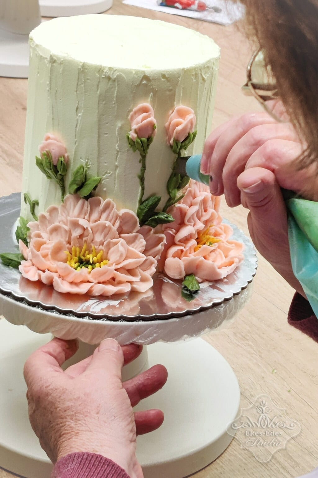 Csokoládékrém virágos torta díszítése közben résztvevő alkot.